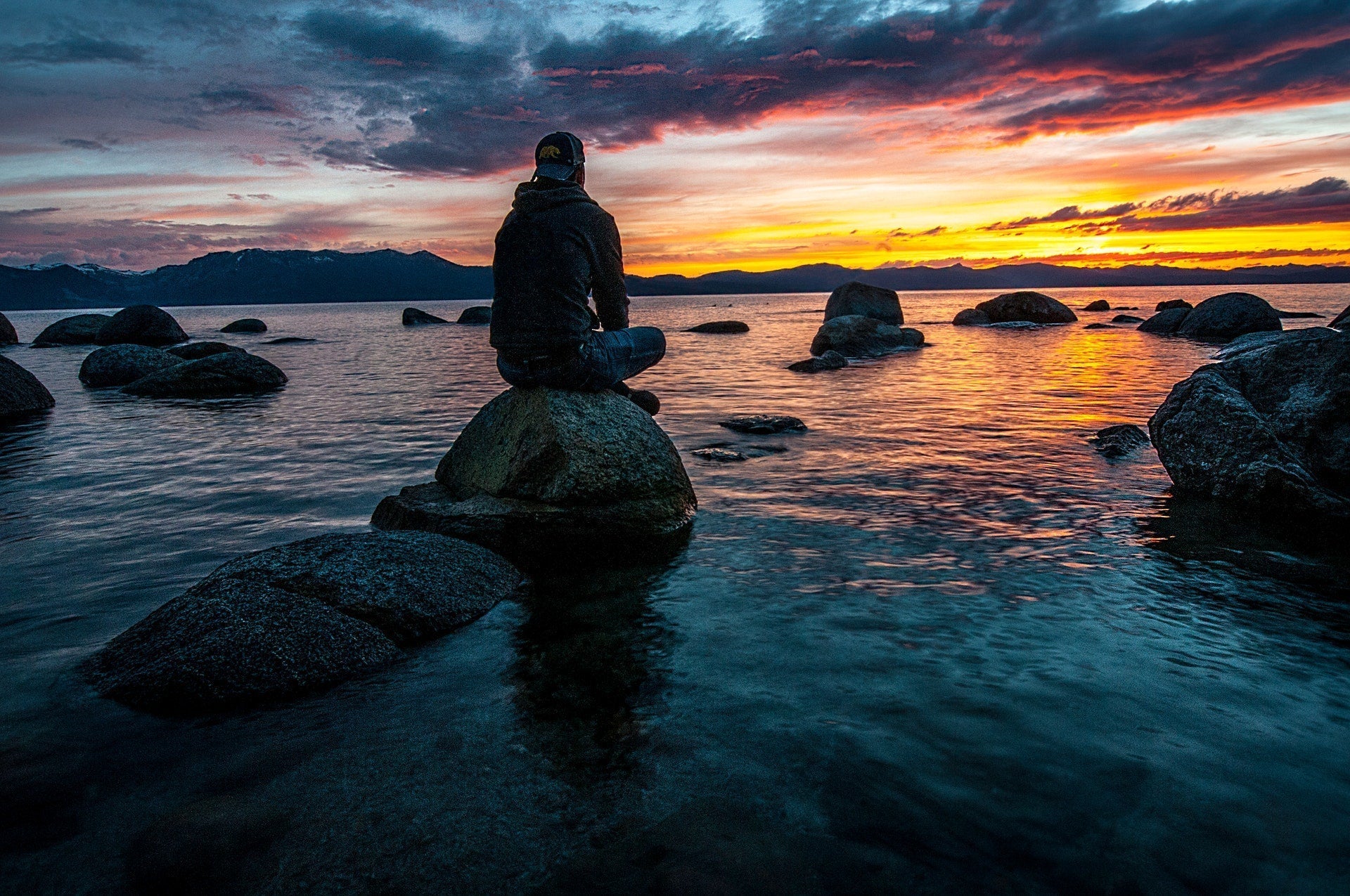 man looking at the ocean sitting on a rock