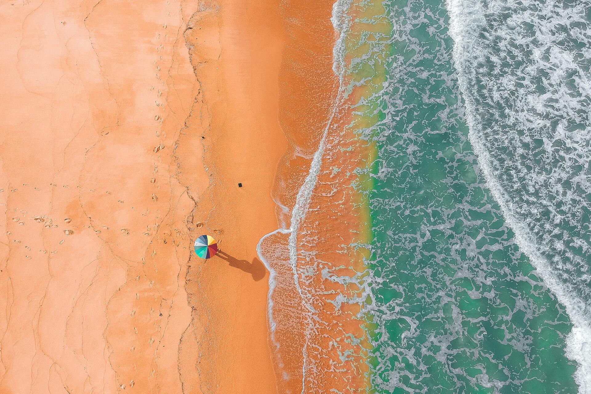 person walking on sand next to ocean